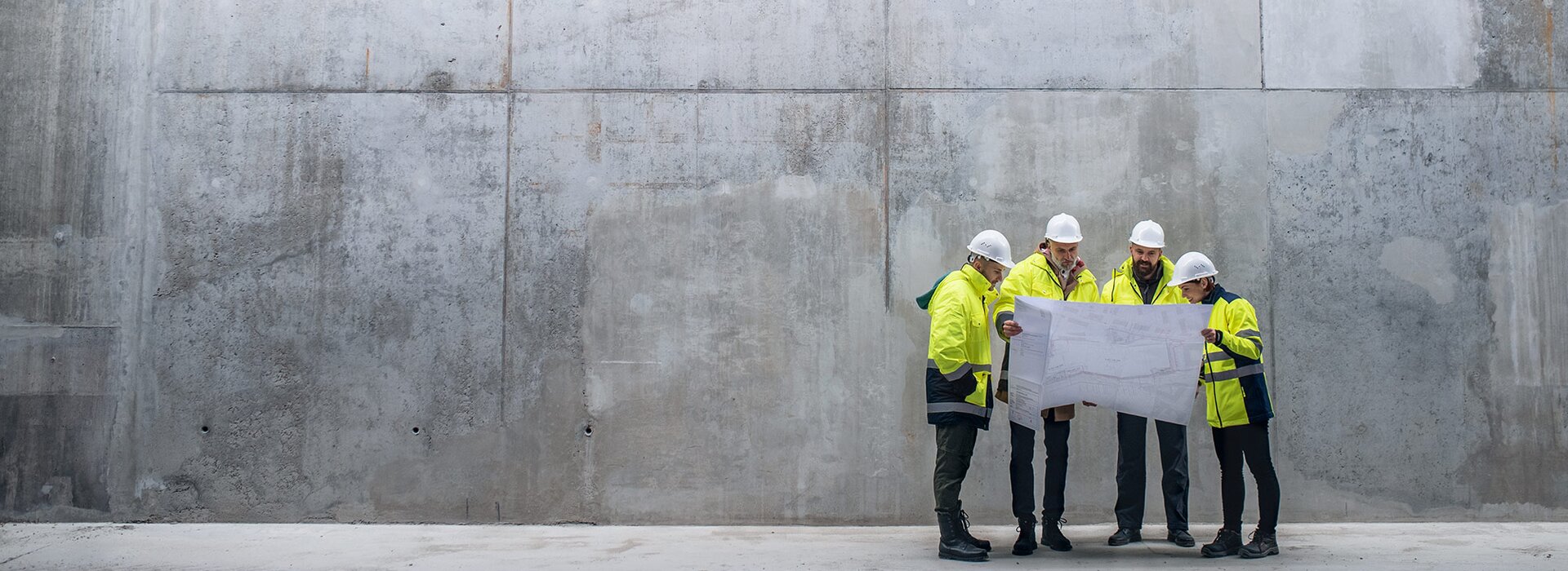 Baustellenbesprechung mit Bauplan an Betonwand Bauarbeiter besprechen Plan mit Helm
