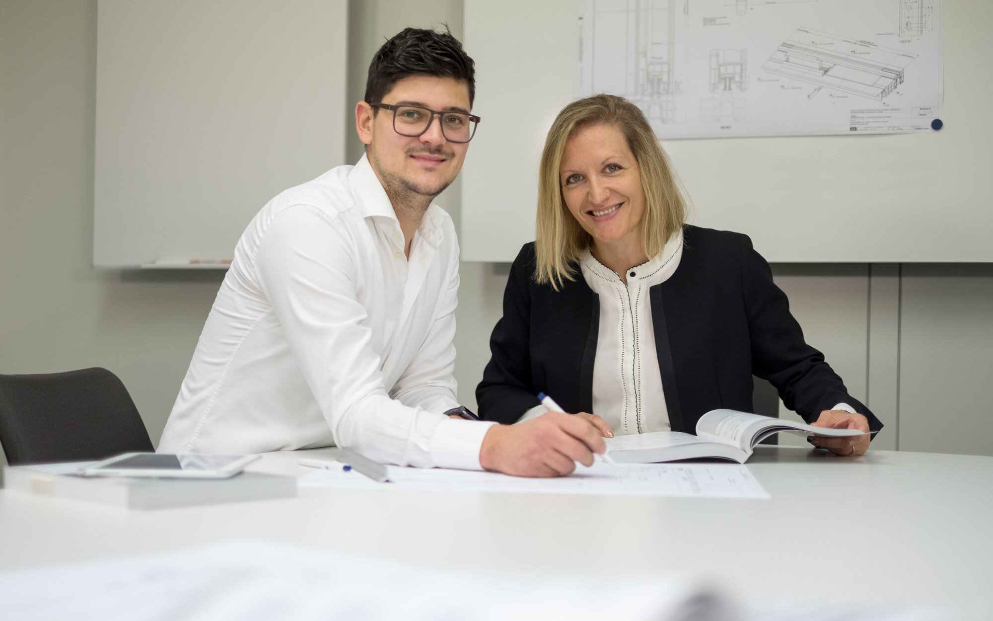 Personen arbeiten an technischen Plänen Zwei Personen arbeiten gemeinsam an technischen Zeichnungen im Büro