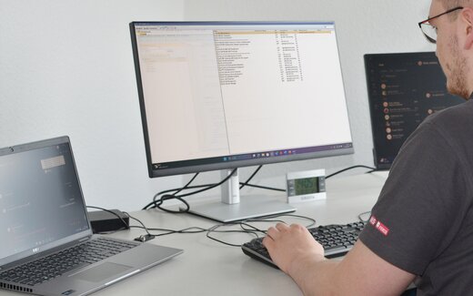 Person an Tastatur vor Computerbildschirm Person am Schreibtisch mit Tastatur und Monitor