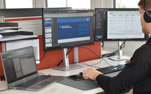 Auswertung Mitarbeiterbefragung im Büro Person arbeitet an Büroarbeitsplatz mit Monitoren