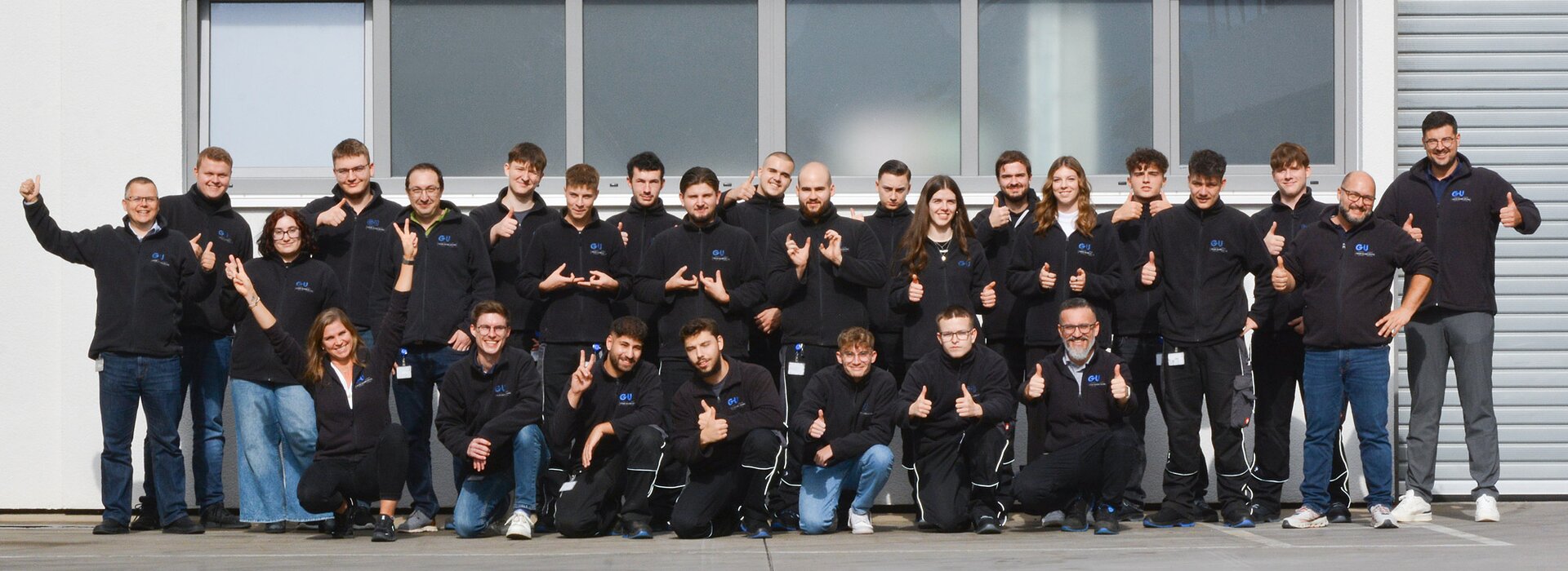 Teamfoto vor Firmengebäude mit Daumen hoch Gruppenfoto eines Teams vor einem Gebäude mit Daumen-hoch-Gesten