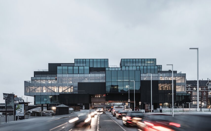 Modernes Glasgebäude mit belebter Straße bei Abend Modernes Bürogebäude mit Glasfassade