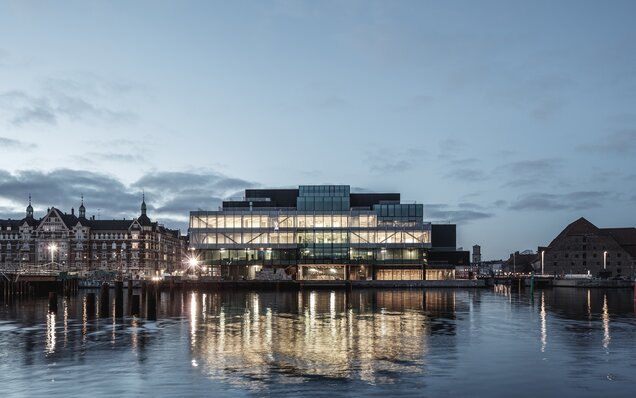 Modernes Gebäude mit Wasserreflexion bei Dämmerung Beleuchtetes Gebäude am Wasser bei Dämmerung
