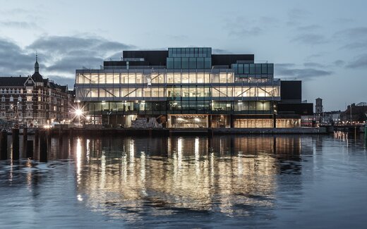 Modernes Glasgebäude am Wasser bei Abenddämmerung Modernes Gebäude mit Glasfassade bei Abend