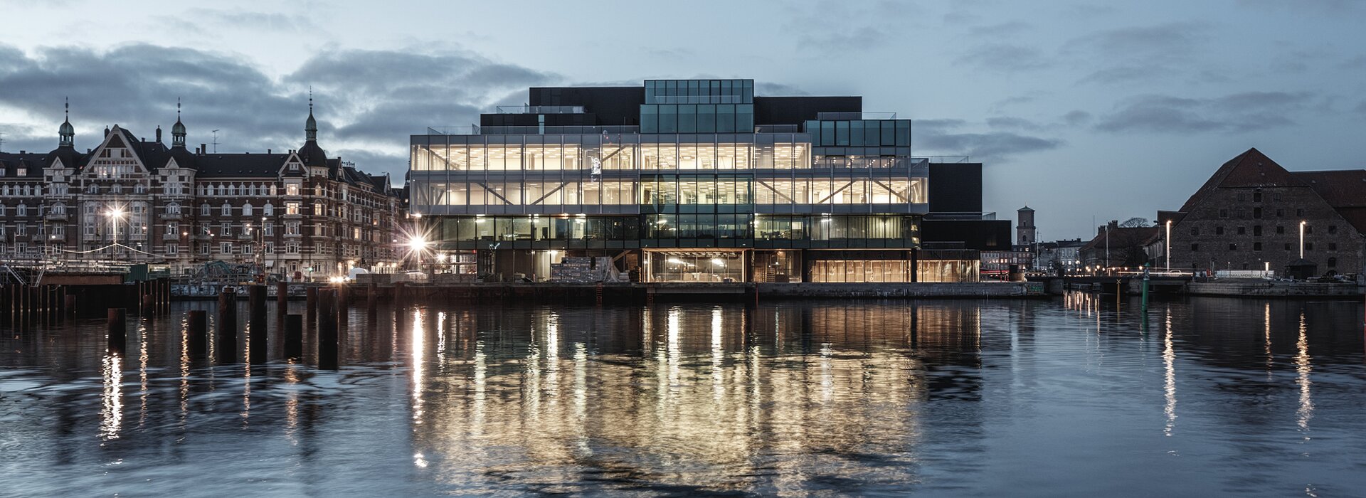 Modernes Glasgebäude am Wasser bei Abenddämmerung Modernes Gebäude mit Glasfassade bei Abend